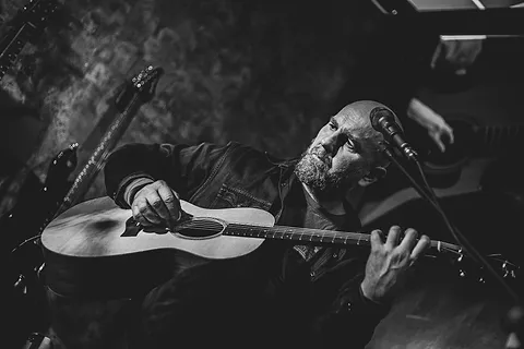 Brodaty gitarzysta gra na gitarze akustycznej przed mikrofonem, ujęcie z góry, czarno-białe zdjęcie z koncertu