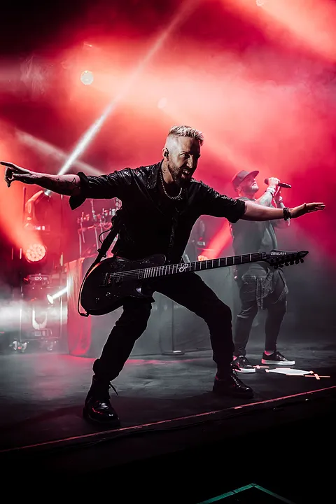 Gitarzysta z rozłożonymi ramionami gra na ośmiostrunowej gitarze w czerwonych światłach