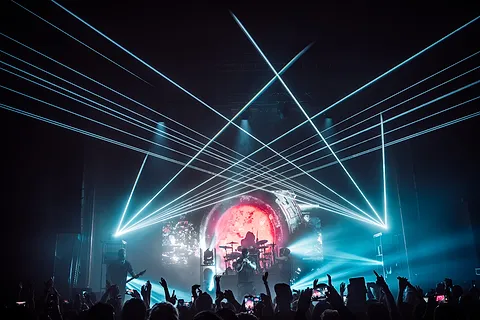 Scena z zespołem w świetle niebieskich laserów, przed sceną tłum publiczności