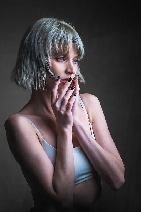 Portret kobiety z krótkimi włosami, dłonie przy twarzy, ujęcie do pasa na ciemnym tle